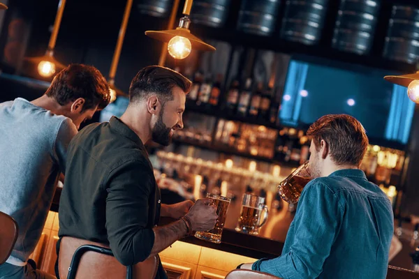 Achteraanzicht van vrolijke jongemannen in casual kleding genietend van bier in pub — Stockfoto