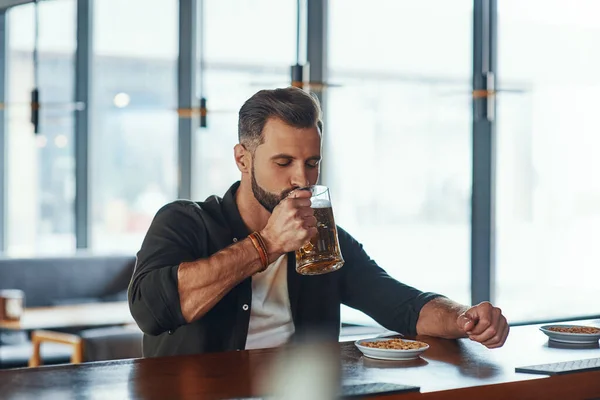 Jovem bonito em roupas casuais bebendo cerveja enquanto passava tempo no pub — Fotografia de Stock