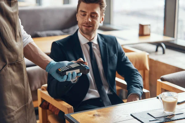 Handsome young businessman making a contactless payment while sitting in the restaurant — Stock Photo, Image