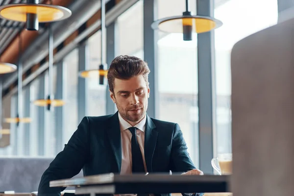 Hezký mladý muž v obleku sedí u stolu v restauraci — Stock fotografie