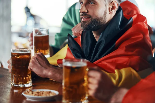 Junge Männer in Nationalflaggen genießen Bier, während sie in der Kneipe ein Sportspiel verfolgen — Stockfoto
