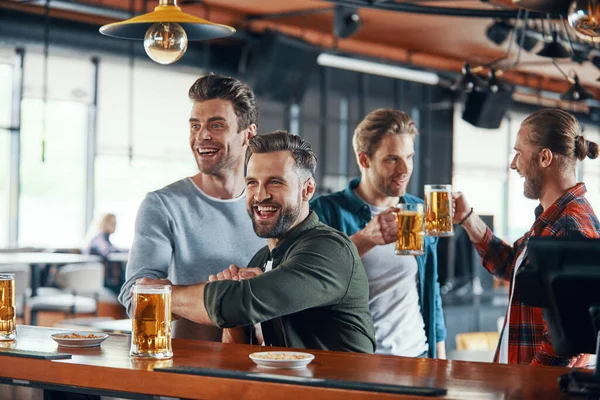 Animando os jovens em roupas casuais assistindo jogo esportivo e curtindo cerveja enquanto sentados no pub — Fotografia de Stock