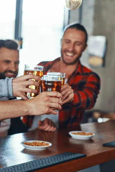 Glada unga män i vardagskläder skålar med öl och ler — Stockfoto