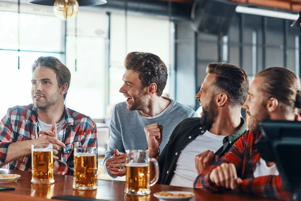 Vrolijke jonge mannen in casual kleding genieten van bier tijdens het zitten in de pub — Stockfoto