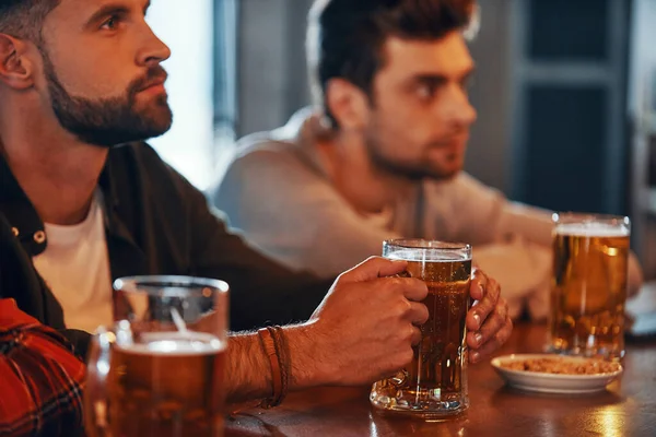 Jovens em roupas casuais desfrutando de cerveja enquanto assistem TV no pub — Fotografia de Stock