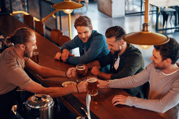 Bovenaanzicht van een barman die bier serveert aan jonge mannen terwijl hij aan de bar in de pub staat — Stockfoto