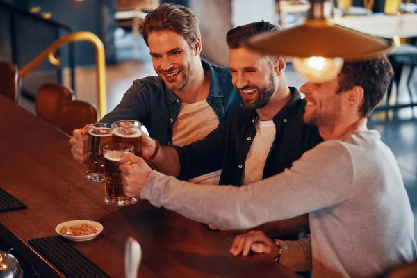 Draufsicht auf glückliche junge Männer, die sich mit Bier anstoßen und lächeln, während sie an der Theke im Pub sitzen — Stockfoto