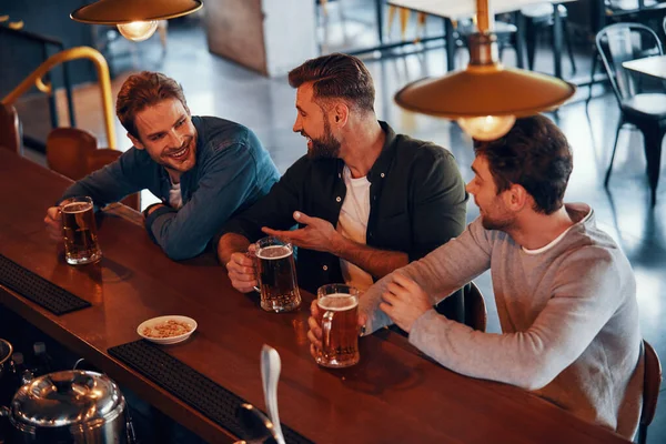 Top view of happy young men in casual clothing talking and enjoying beer — Stock Photo, Image