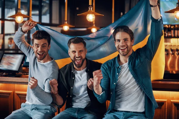 Tři jásající mladí muži s ukrajinskou vlajkou a s úsměvem — Stock fotografie
