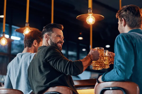 Rückansicht glücklicher junger Männer in lässiger Kleidung, die mit Bier anstoßen — Stockfoto