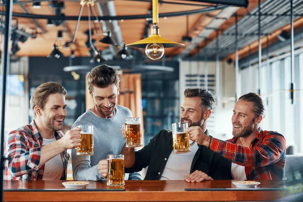 Jovens felizes em roupas casuais brindando uns aos outros com cerveja e sorrindo — Fotografia de Stock