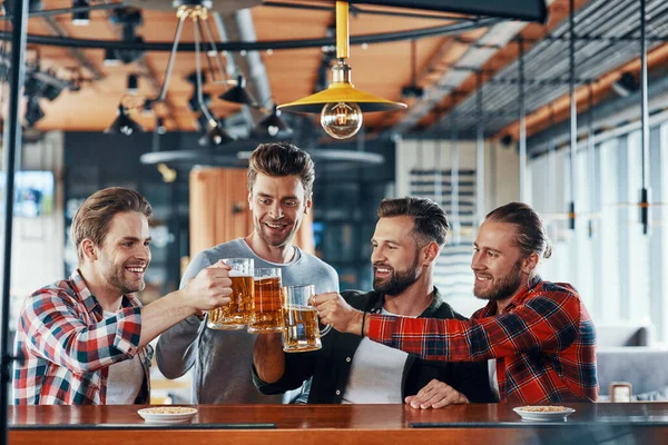 Groep gelukkige jonge mannen in casual kleding toasten op elkaar met bier en glimlachen — Stockfoto