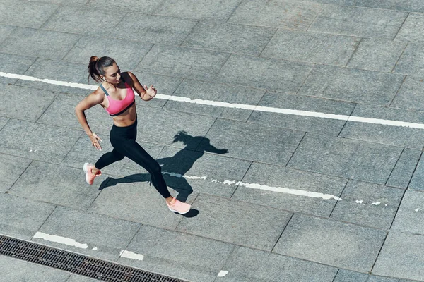 Top view of confident young woman in sports clothing running outdoors — Stock Photo, Image