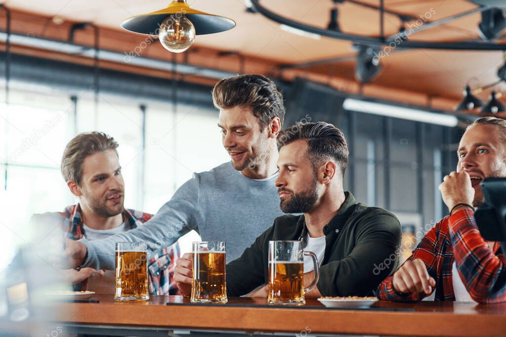 Group of young men in casual clothing enjoying beer and communicating