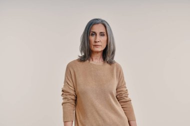 Olgun, güzel bir kadın gri arka planda kameraya bakıyor.