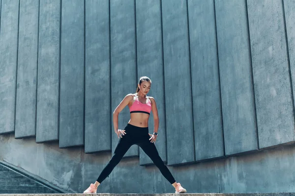 Comprimento total de jovem mulher confiante em sportswear exercício ao ar livre — Fotografia de Stock