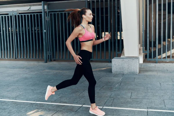 Comprimento total de bela jovem mulher em roupas esportivas correndo ao ar livre — Fotografia de Stock