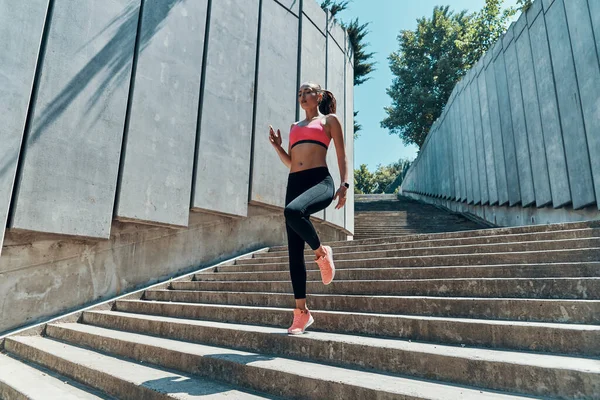 Όμορφη νεαρή γυναίκα με αθλητικά ρούχα τρέχει κάτω στο ύπαιθρο — Φωτογραφία Αρχείου
