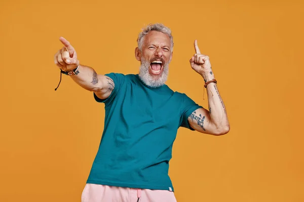 Happy senior man keeping arms outstretched and shouting while standing against orange background — Stock Photo, Image