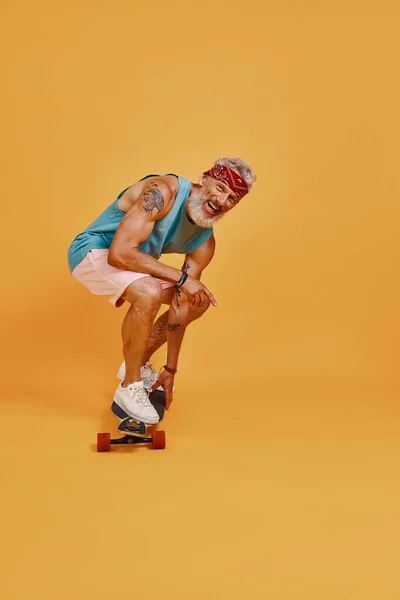 Volledige lengte van actieve senior skateboarden tegen oranje achtergrond — Stockfoto