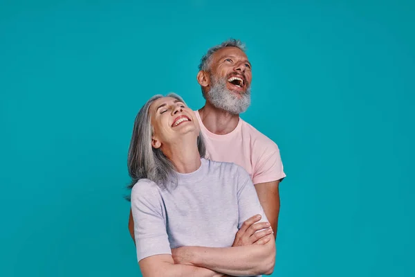 Glad senior par bindning och skratta när du står tillsammans mot blå bakgrund — Stockfoto