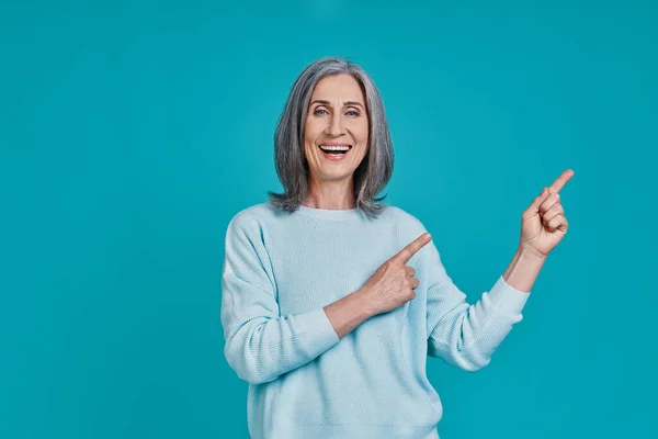 Mature beautiful woman looking at camera and smiling while standing against blue background — Stock Photo, Image