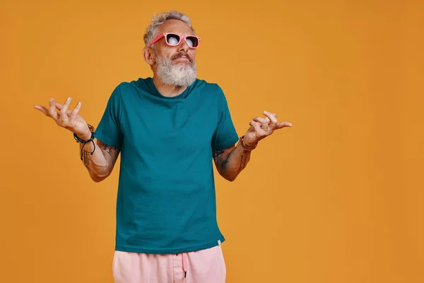 Funky hombre mayor encogiéndose de hombros mientras está de pie sobre fondo naranja — Foto de Stock