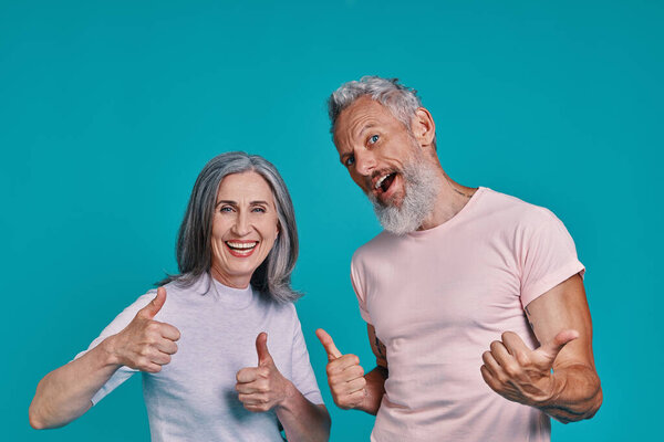 Beautiful senior couple looking at camera and keeping thumbs up