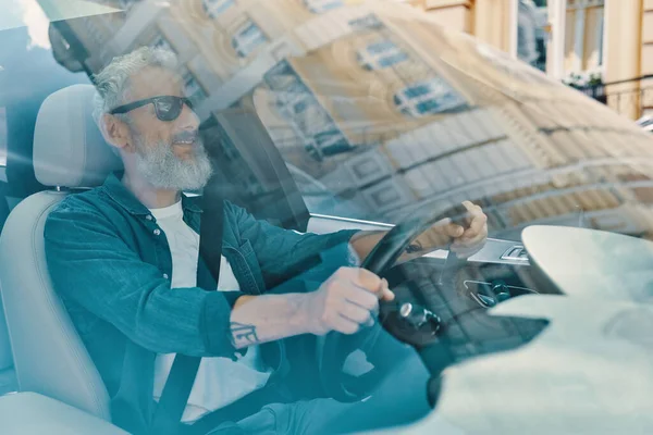 Homme âgé actif en vêtements décontractés profitant d'une promenade en voiture tout en étant assis sur le siège avant de la voiture — Photo