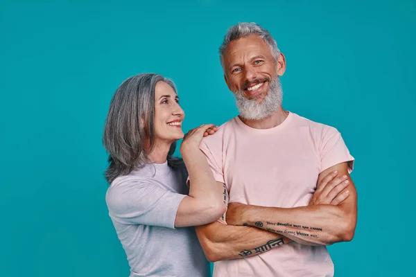 Mooi senior paar op zoek naar camera en glimlachen terwijl samen staan tegen een blauwe achtergrond — Stockfoto