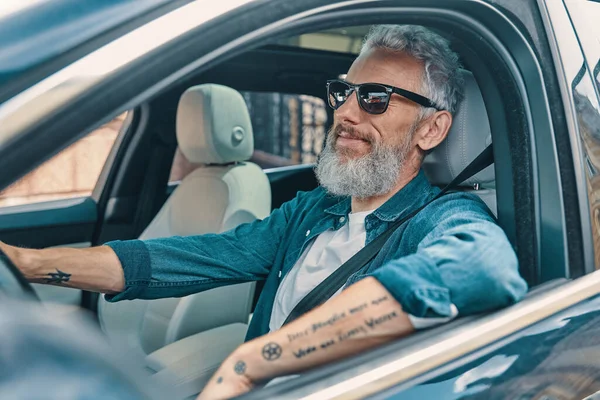 Active senior man in casual clothing enjoying car ride while sitting on front seat of the car — Stock Photo, Image