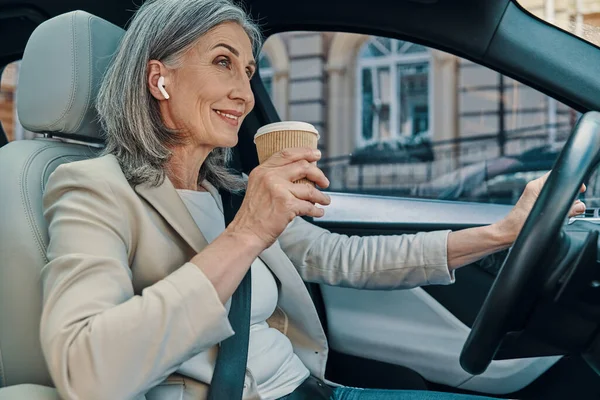 Mature belle femme en smart casual porter souriant et boire du café tout en conduisant voiture — Photo