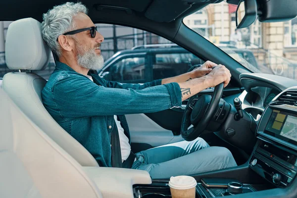 Schöner älterer Mann in lässiger Kleidung genießt Autofahrt, während er auf dem Vordersitz des Autos sitzt — Stockfoto