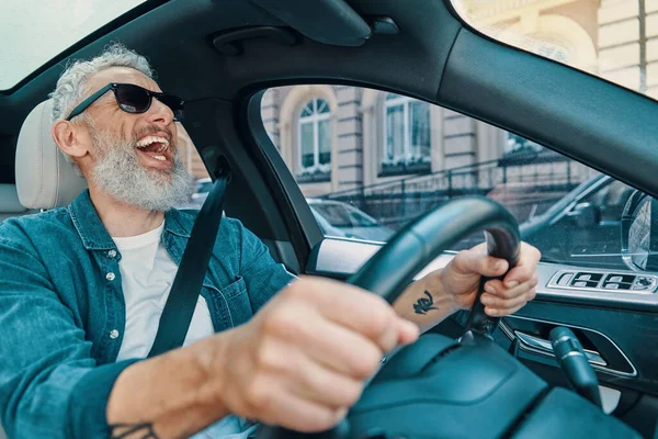 Heureux homme âgé en vêtements décontractés profiter de balade en voiture et rire tout en étant assis sur le siège avant de la voiture — Photo