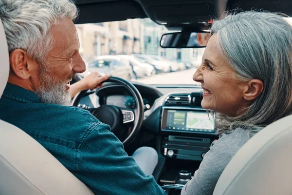 Rückansicht eines aktiven Seniorehepaares, das die Autofahrt genießt, während es auf den Vordersitzen des Autos sitzt — Stockfoto