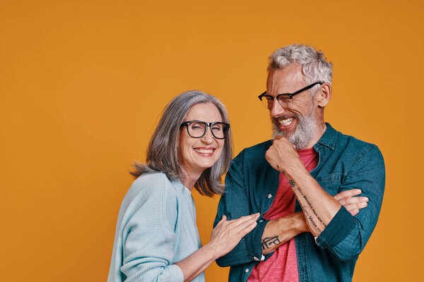 Happy senior couple smiling while standing together against orange background