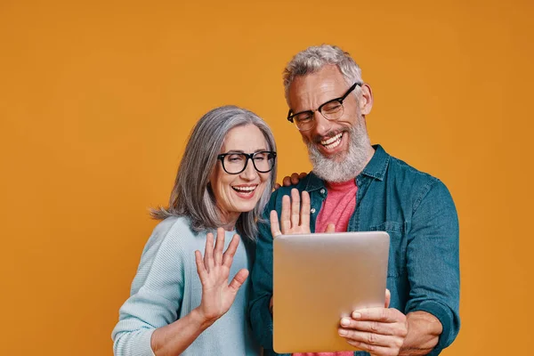 Glückliches Seniorenpaar lächelt und nutzt digitales Tablet und winkt — Stockfoto