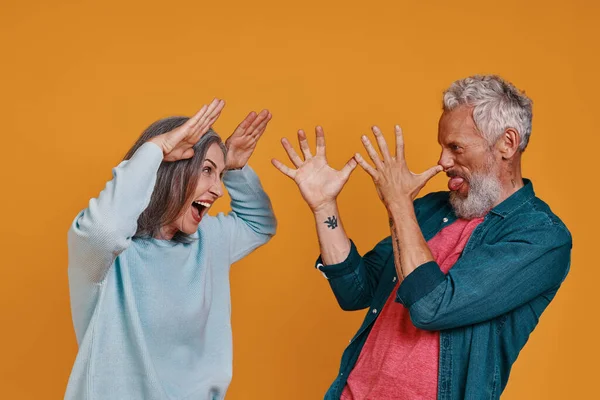 Zabawna para starszych gestykulując i robiąc twarze stojąc razem na pomarańczowym tle — Zdjęcie stockowe