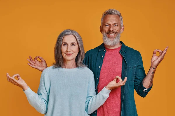 Vackra senior par mediterar och ler när de står tillsammans mot orange bakgrund — Stockfoto