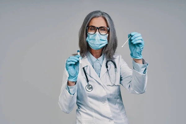 Mature beautiful female doctor in face mask looking at camera and holding medical test — Stock Photo, Image