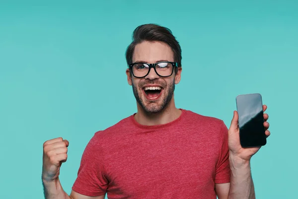 Ritratto di bel giovane uomo sorridente con gli occhiali che mostra il suo smartphone e gesticolando — Foto Stock