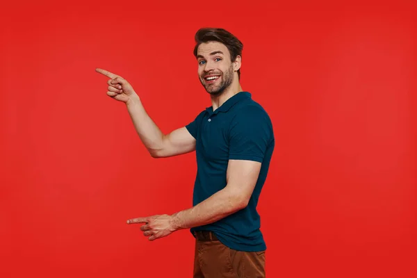 Happy young man in casual wear looking at camera and pointing away — Stock Photo, Image