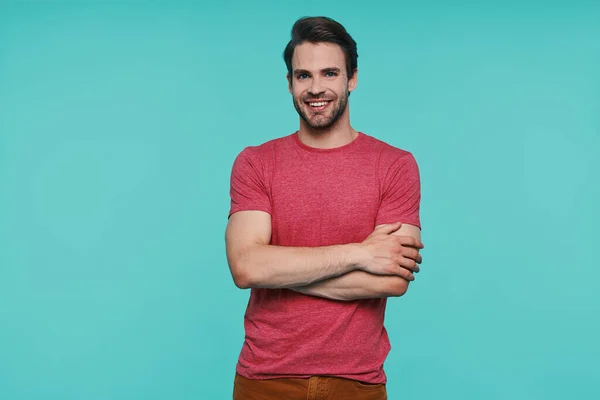 Bonito jovem sorrindo homem em roupas casuais olhando para a câmera e mantendo os braços cruzados — Fotografia de Stock