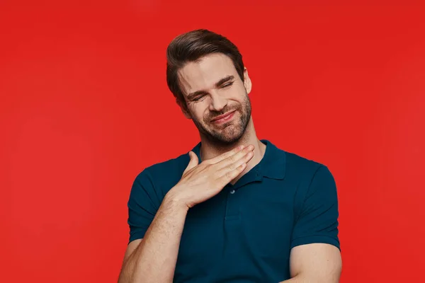 Displeased young man in casual wear making a face and gesturing while standing against red background — Stock Photo, Image