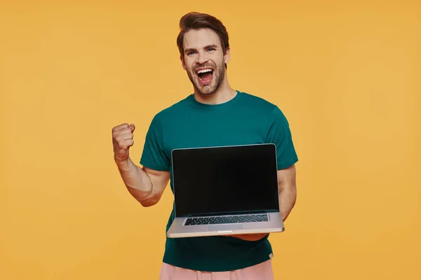Bello giovane uomo sorridente in abbigliamento casual che trasporta laptop e gesti — Foto Stock