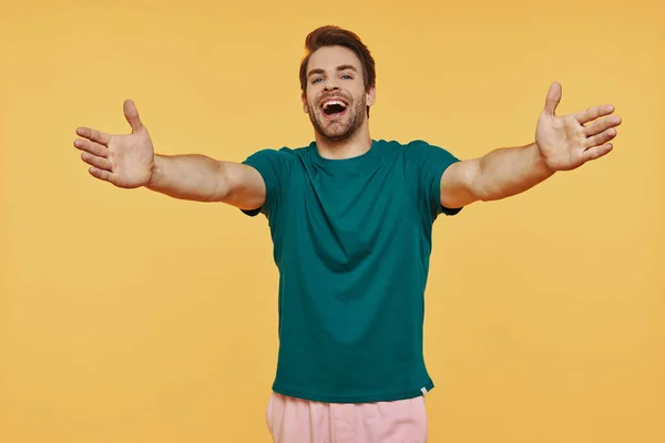 Šťastný mladý usměvavý muž v neformálním oblečení dívající se na kameru a gestikulující objetí — Stock fotografie