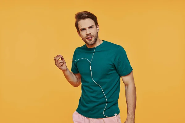 Frustrovaný mladý muž ve sluchátkách při pohledu na kameru, zatímco stojí na žlutém pozadí — Stock fotografie