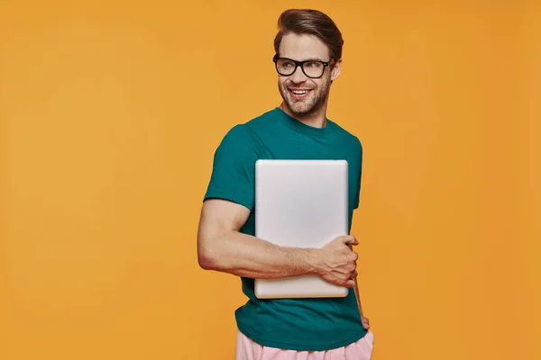 Stilig ung man i avslappnade kläder bär laptop och ler — Stockfoto