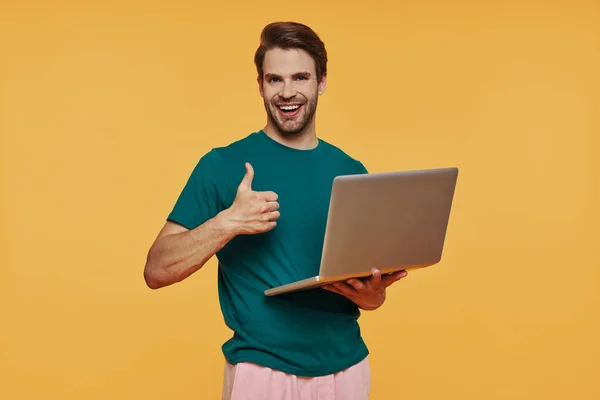 Красивый молодой улыбающийся мужчина в повседневной одежде с ноутбуком и жестом — стоковое фото