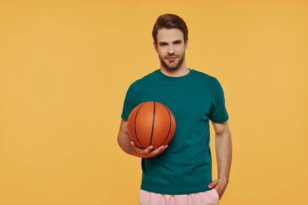 Hezký mladý muž drží basketbal a dívá se na kameru — Stock fotografie